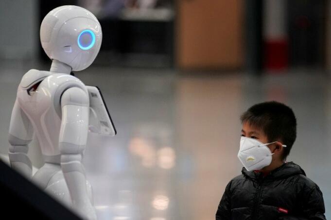 Seorang anak lelaki memperhatikan robot sambil memakai masker di Bandara Internasional Pudong di Shanghai, China, Senin (27/1/2020). (REUTERS/ALY SONG)