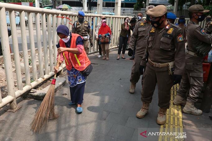 Satpol PP Jakarta Pusat memberikan sanksi kepada pelanggar aturan PSBB untuk memakai rompi oranye dan membersihkan fasilitas umum di kawasan Tanah Abang, Jakarta, Rabu (13/5/2020). ANTARA/Sugiharto Purnama/am.